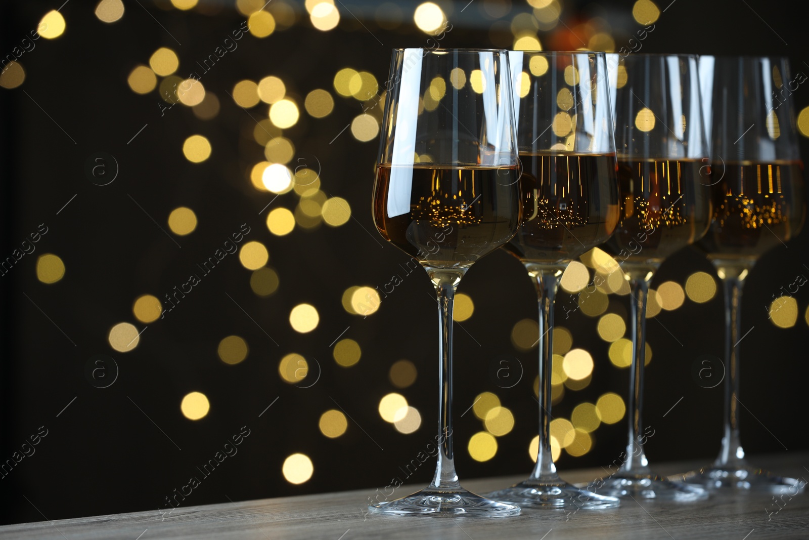 Photo of Glasses of luxury white wine on table against blurred lights, bokeh effect. Space for text