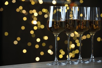 Photo of Glasses of luxury white wine on table against blurred lights, bokeh effect. Space for text