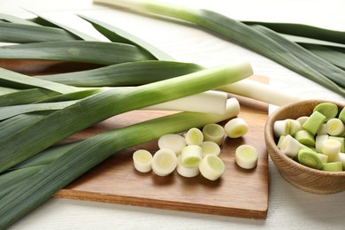 Photo of Whole and cut fresh leeks on white wooden table, closeup