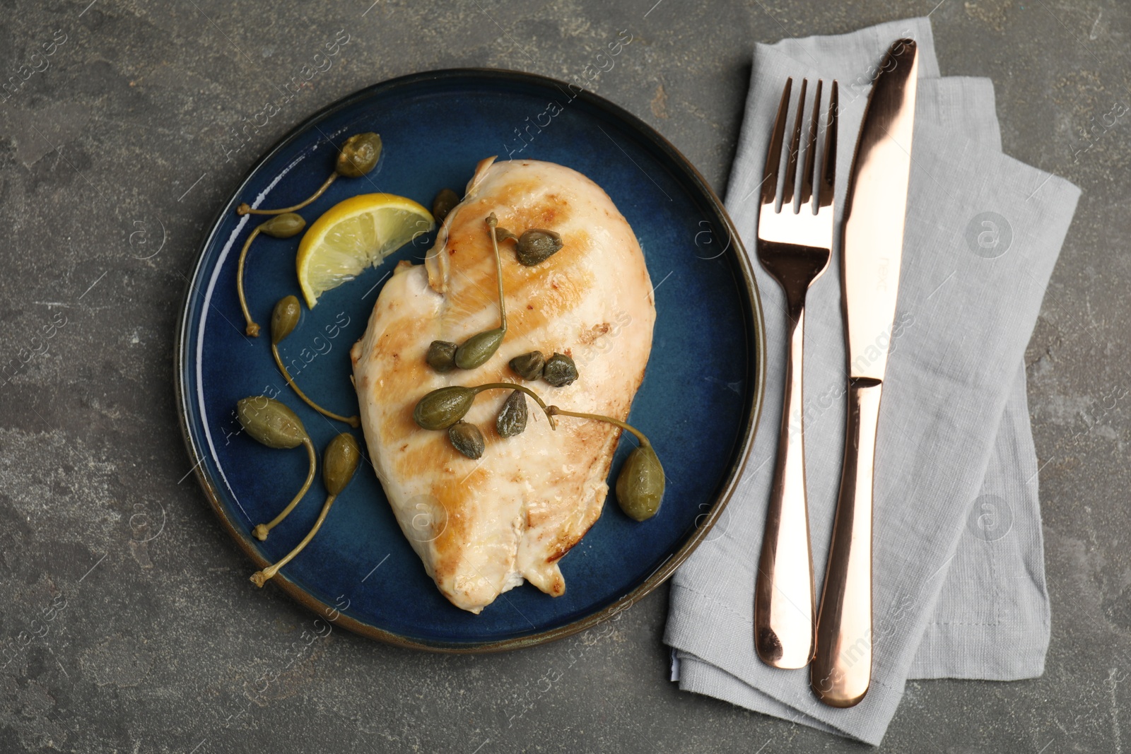 Photo of Delicious cooked chicken fillet with capers and lemon slice served on grey table, flat lay