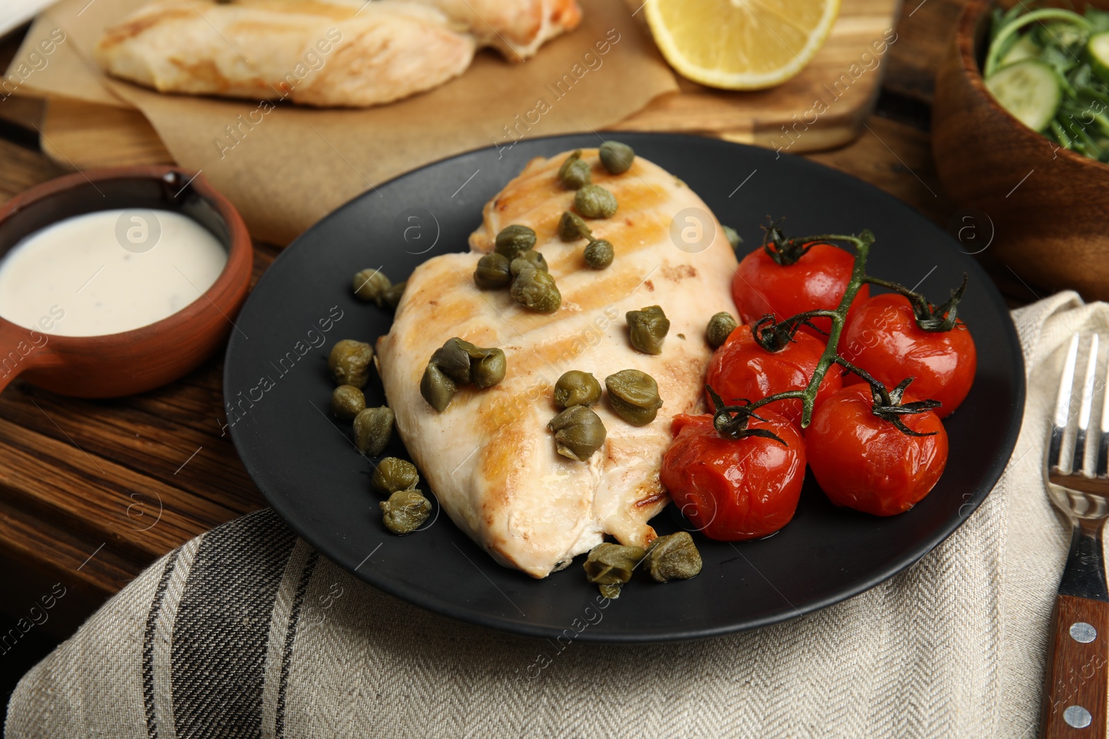 Photo of Delicious cooked chicken fillet with capers and tomatoes served on wooden table