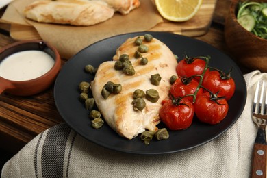 Photo of Delicious cooked chicken fillet with capers and tomatoes served on wooden table