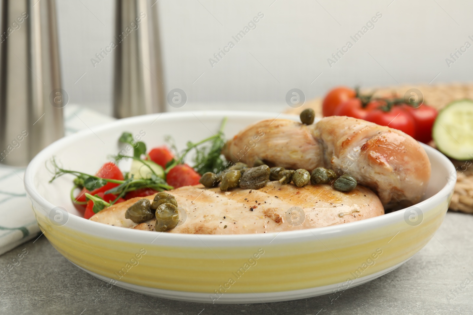 Photo of Delicious cooked chicken fillets with capers and salad on light grey table, closeup