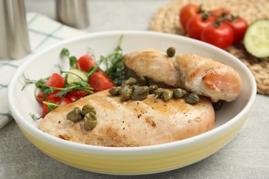 Photo of Delicious cooked chicken fillets with capers and salad on light grey table, closeup