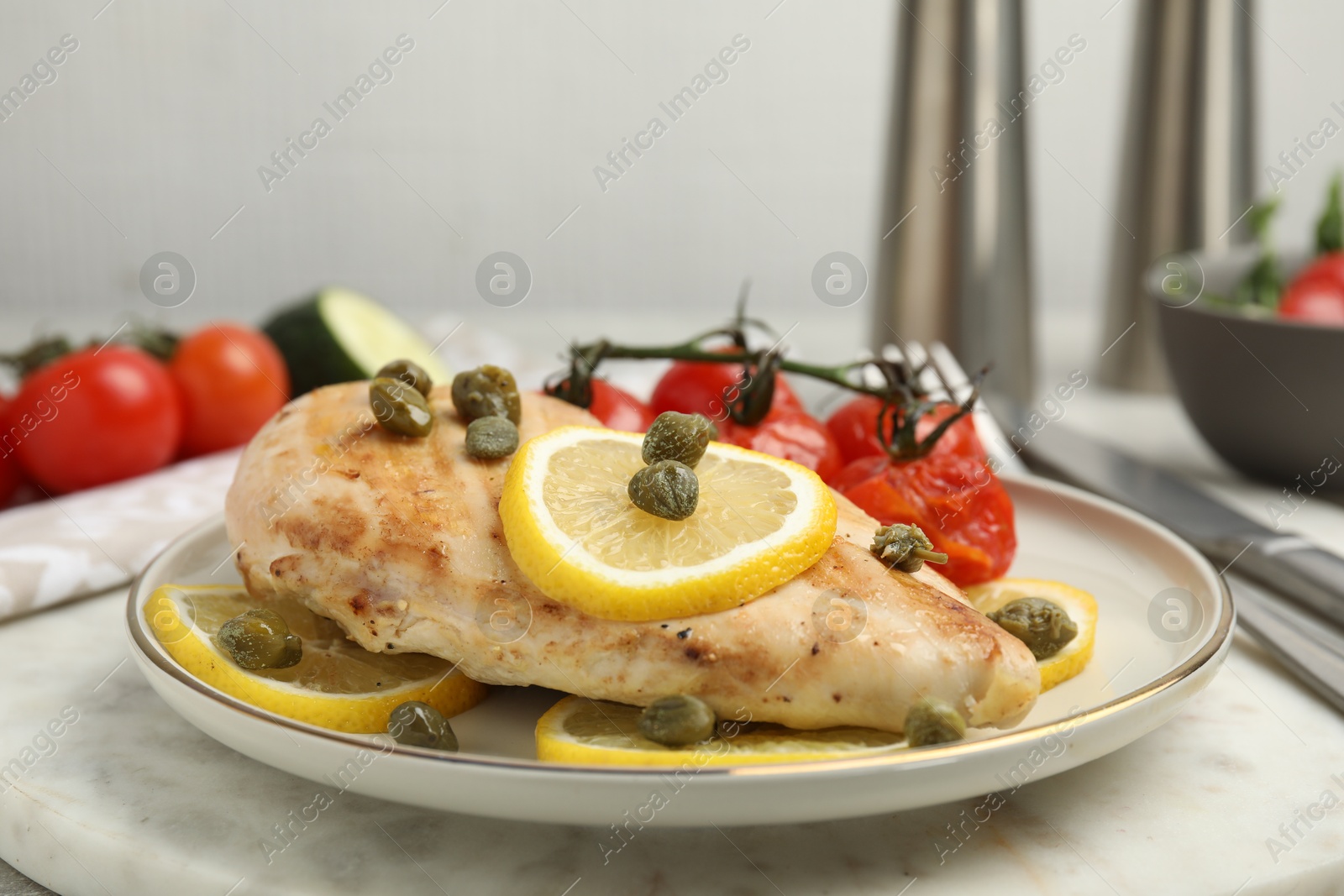 Photo of Delicious cooked chicken fillet with capers, tomatoes and lemon on table, closeup