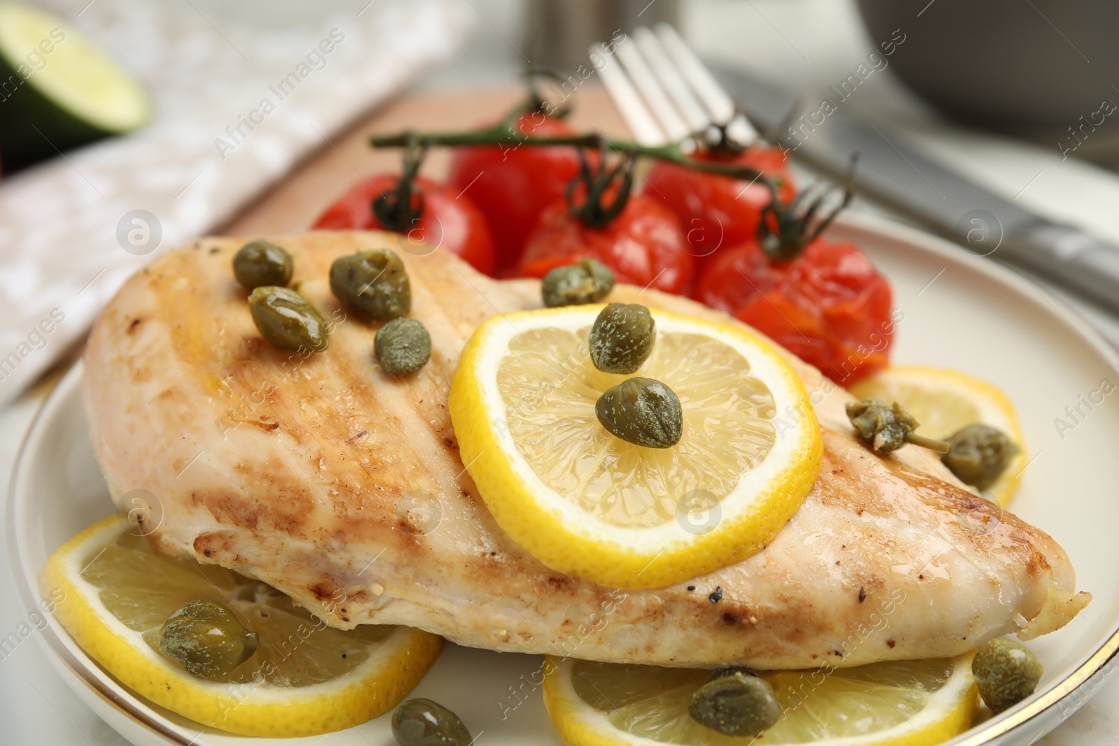 Photo of Delicious cooked chicken fillet with capers, tomatoes and lemon on table, closeup