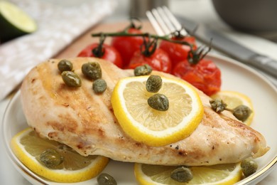 Photo of Delicious cooked chicken fillet with capers, tomatoes and lemon on table, closeup