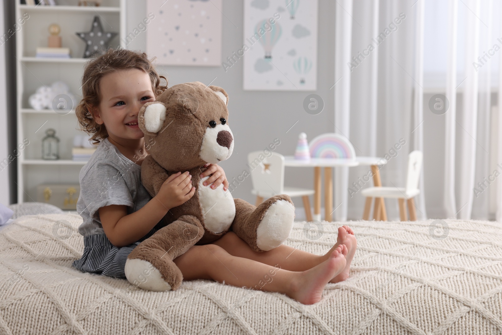 Photo of Cute little girl with teddy bear on bed at home