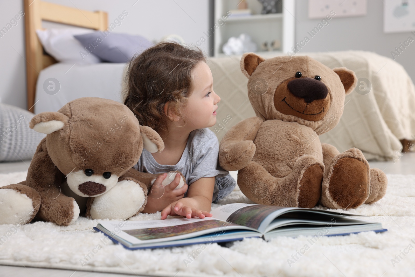 Photo of Cute little girl reading book and teddy bears on floor at home