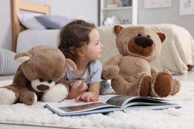 Photo of Cute little girl reading book and teddy bears on floor at home