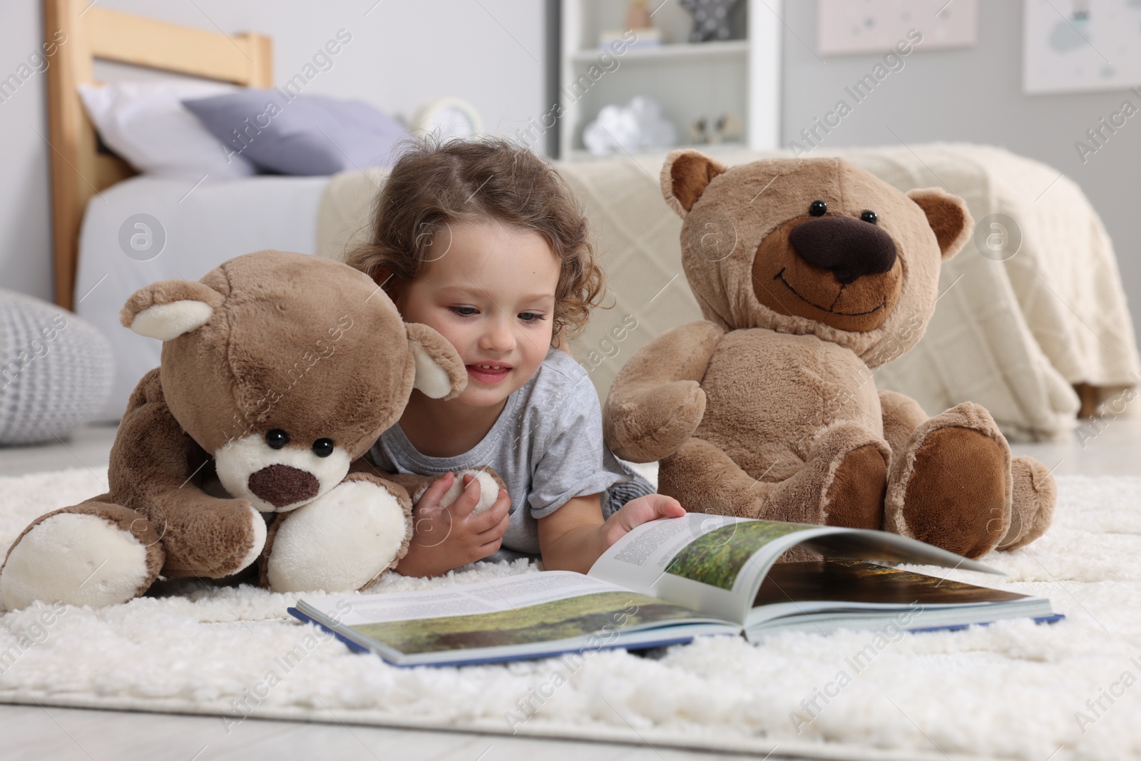 Photo of Cute little girl reading book and teddy bears on floor at home