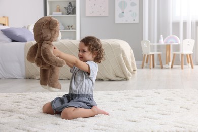 Photo of Cute little girl playing with teddy bear on floor at home