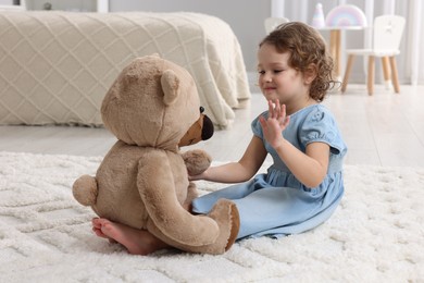 Photo of Cute little girl playing with teddy bear on floor at home