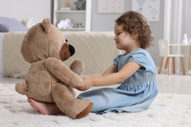 Photo of Cute little girl with teddy bear on floor at home