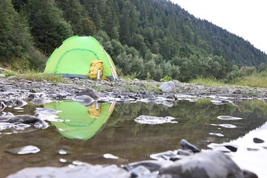 Photo of Camping tent, backpack and thermo bottle on stones near river in mountains