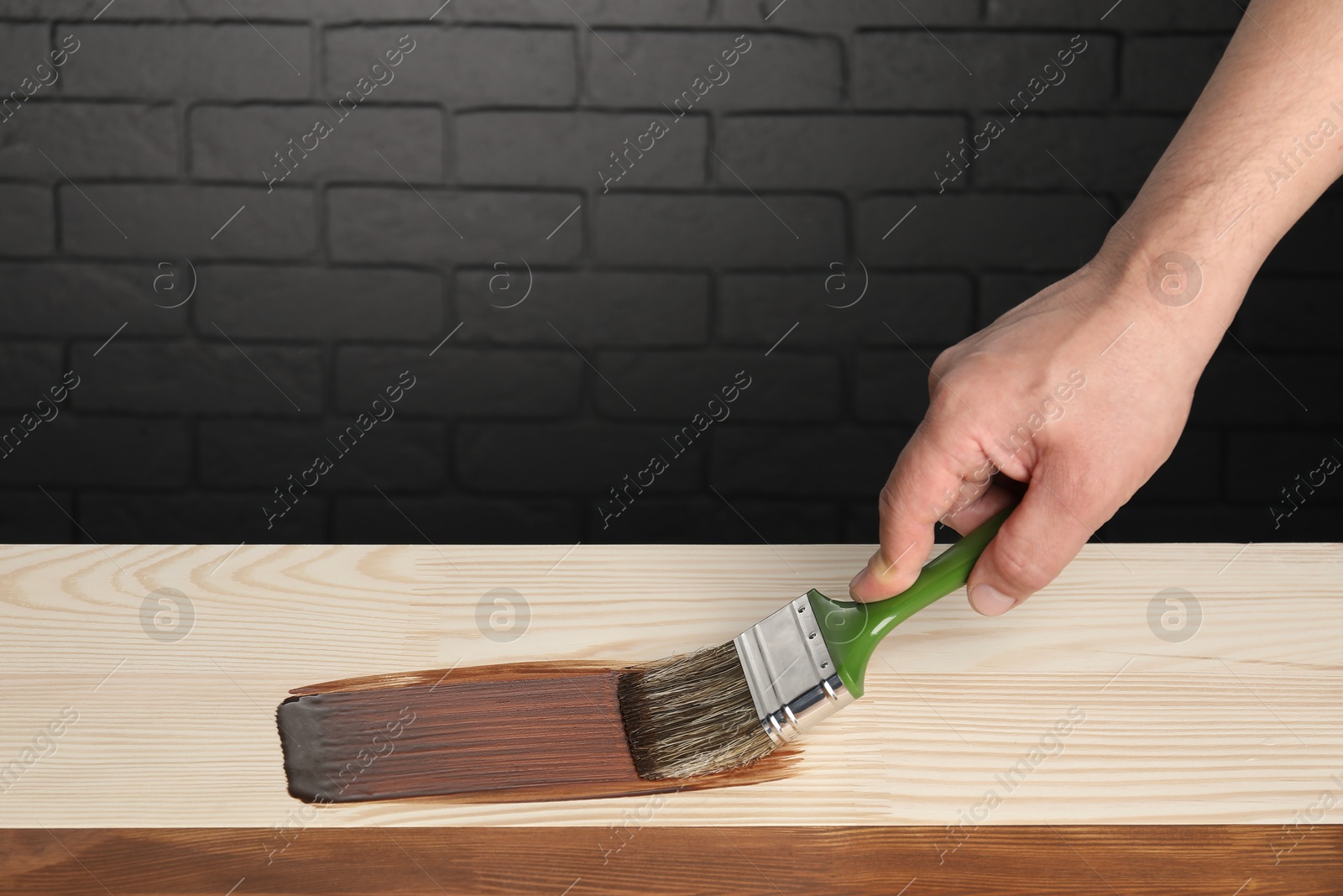 Photo of Man with brush applying walnut wood stain onto wooden surface, closeup