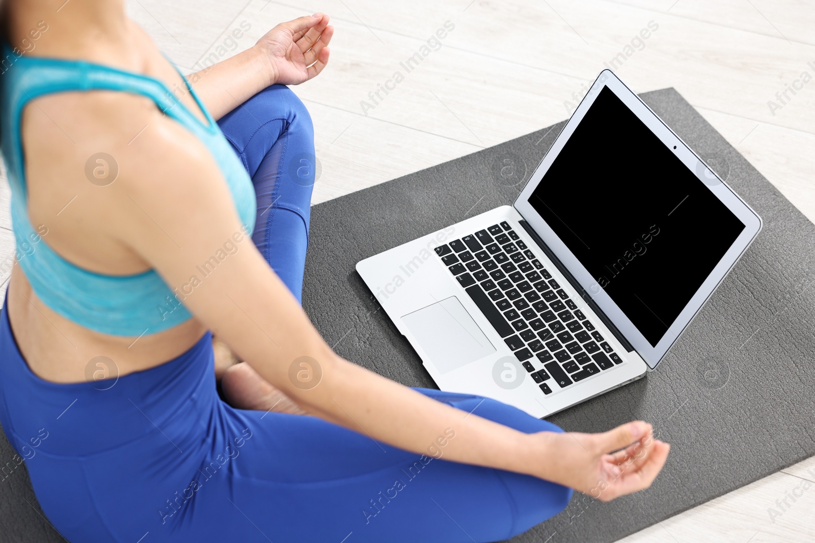 Photo of Woman meditating near laptop on yoga mat at home, closeup