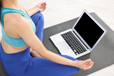 Woman meditating near laptop on yoga mat at home, closeup