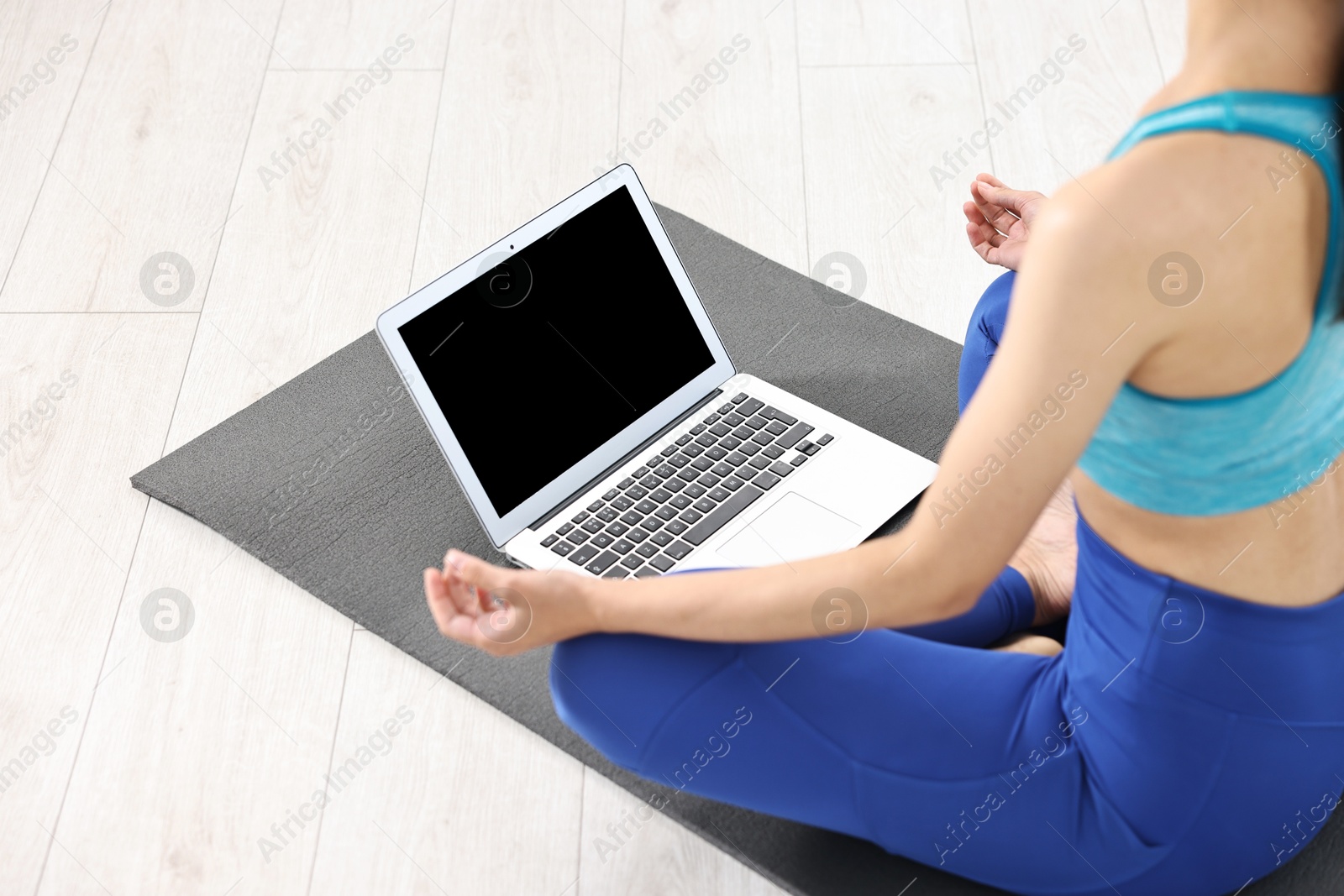 Photo of Woman meditating near laptop on yoga mat at home, closeup