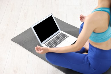 Woman meditating near laptop on yoga mat at home, closeup