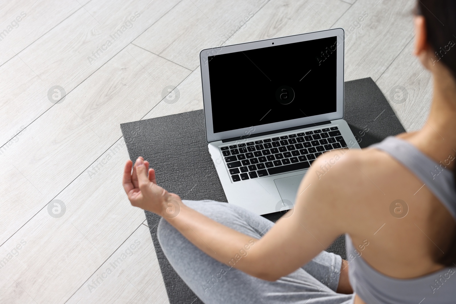 Photo of Woman meditating near laptop on yoga mat at home, closeup