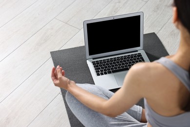 Woman meditating near laptop on yoga mat at home, closeup