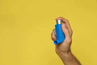 Photo of Man holding asthma inhaler on yellow background, closeup. Space for text