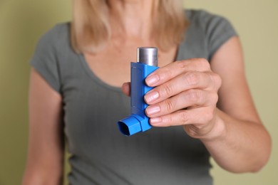 Photo of Woman holding asthma inhaler on olive background, closeup