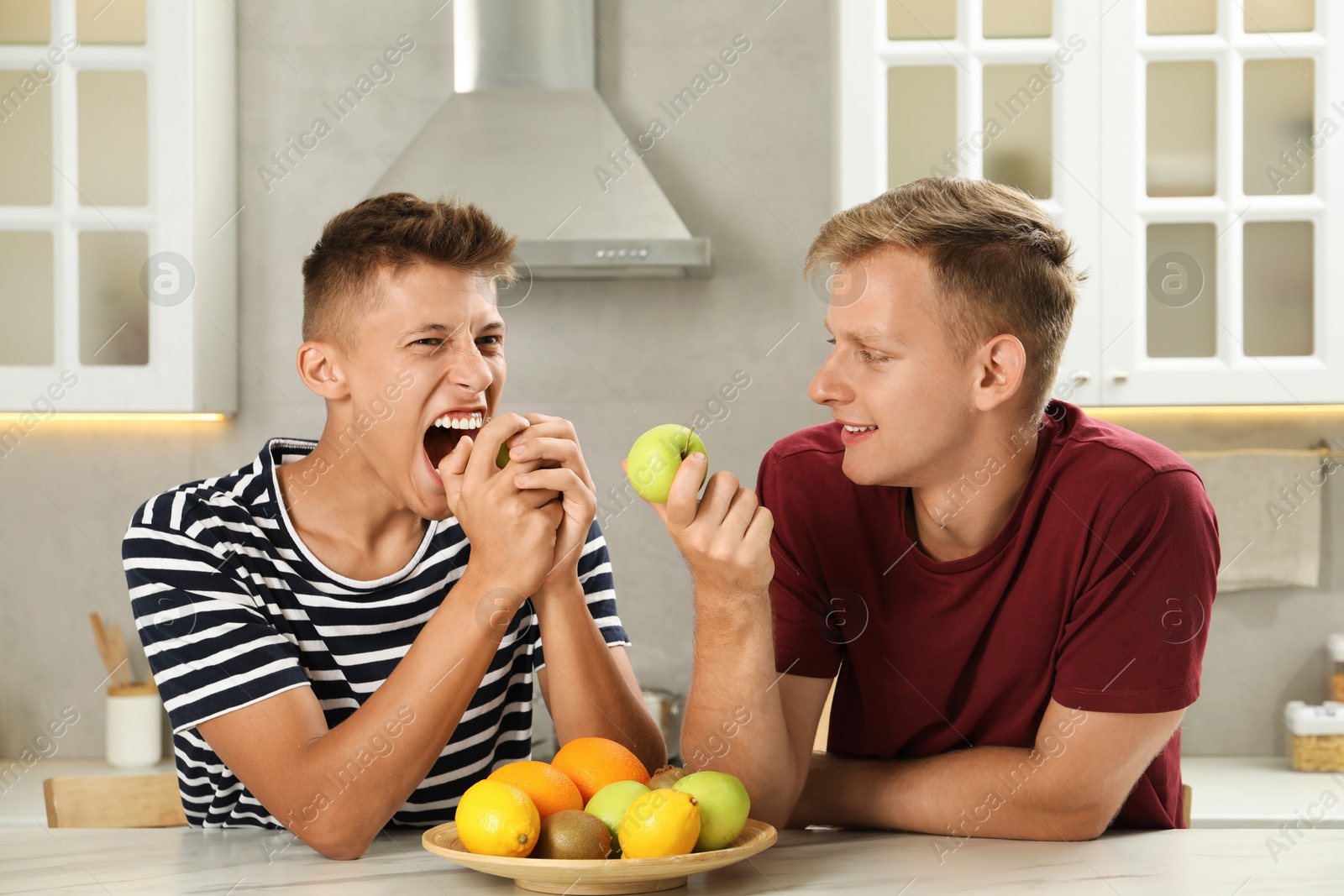 Photo of Happy brothers eating apples at table in kitchen