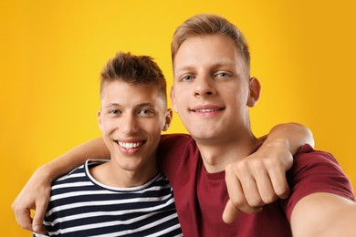 Happy brothers taking selfie on orange background