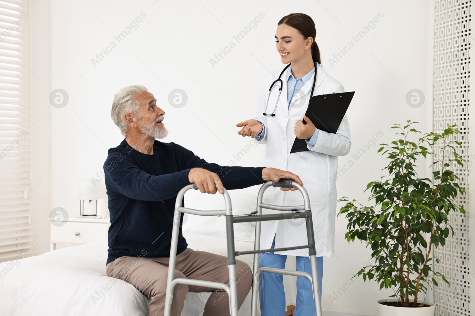 Photo of Doctor consulting senior patient with walking frame in hospital ward