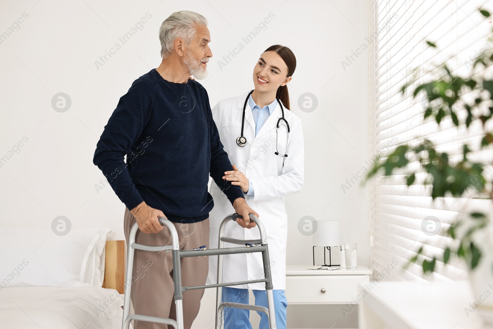 Photo of Doctor helping senior man with walking frame in clinic