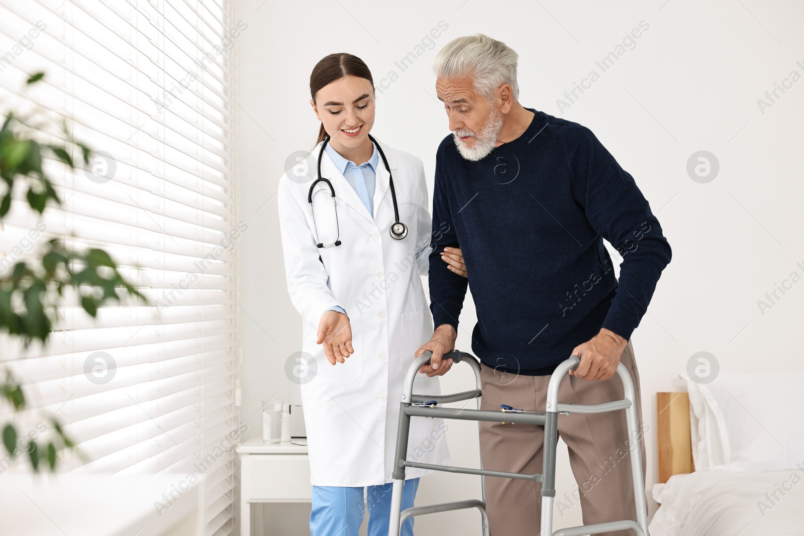 Photo of Doctor helping senior man with walking frame in clinic