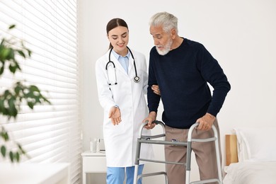 Photo of Doctor helping senior man with walking frame in clinic