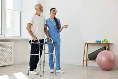 Nurse helping senior man with walking frame in clinic