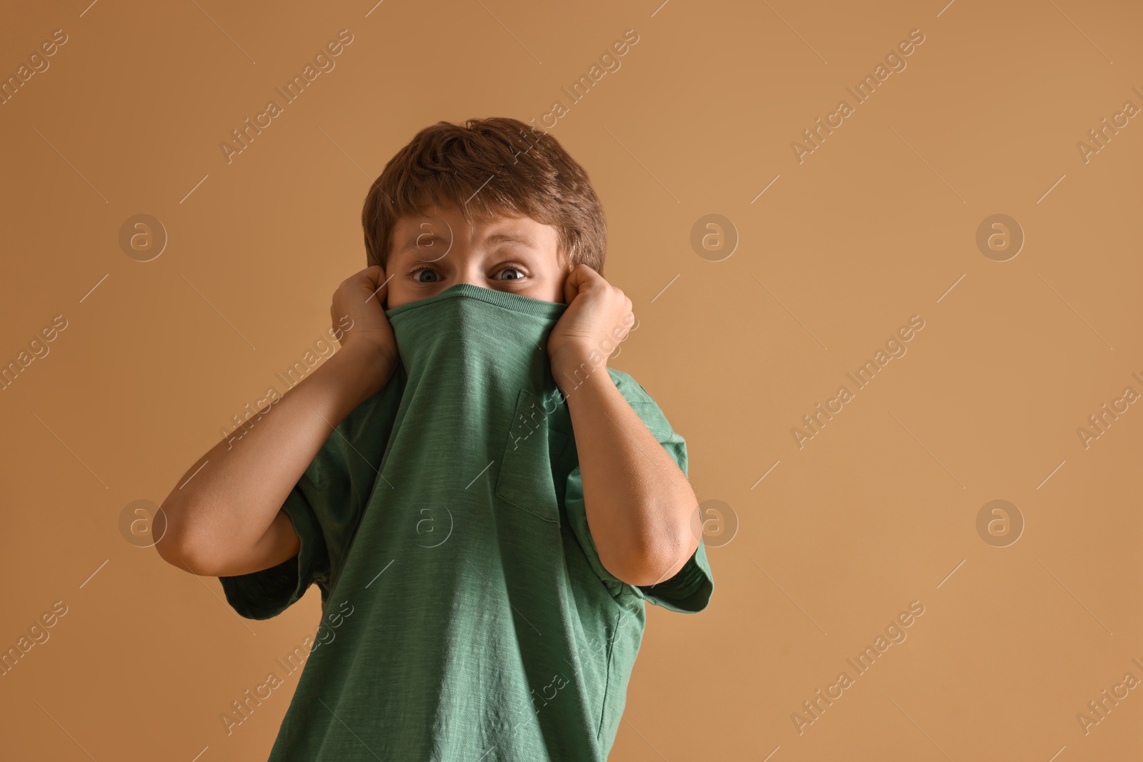 Photo of Scared little boy hiding on beige background. Space for text