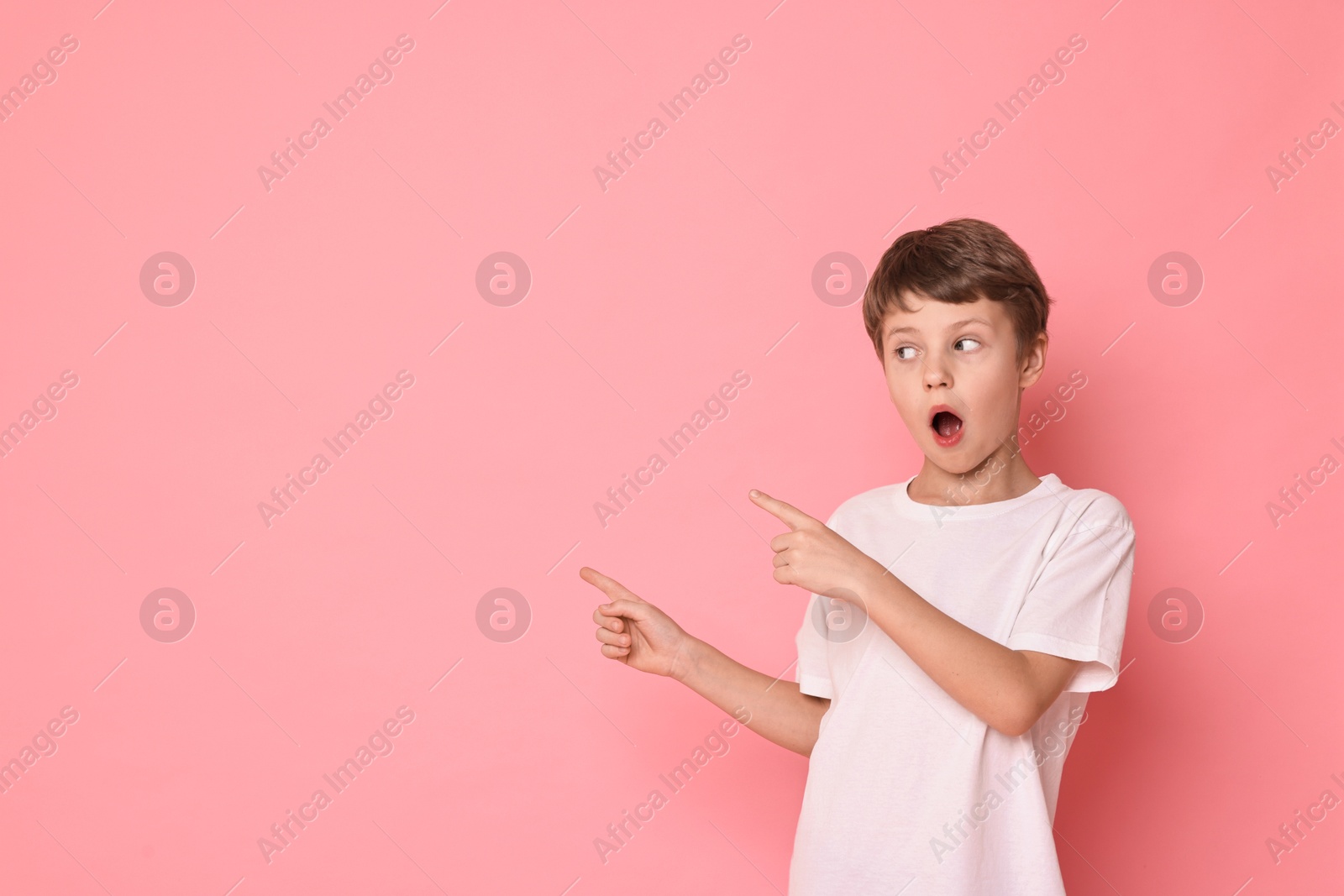 Photo of Portrait of scared little boy pointing at something on pink background. Space for text