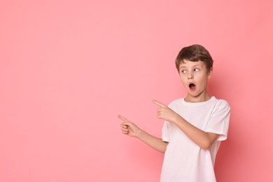 Portrait of scared little boy pointing at something on pink background. Space for text