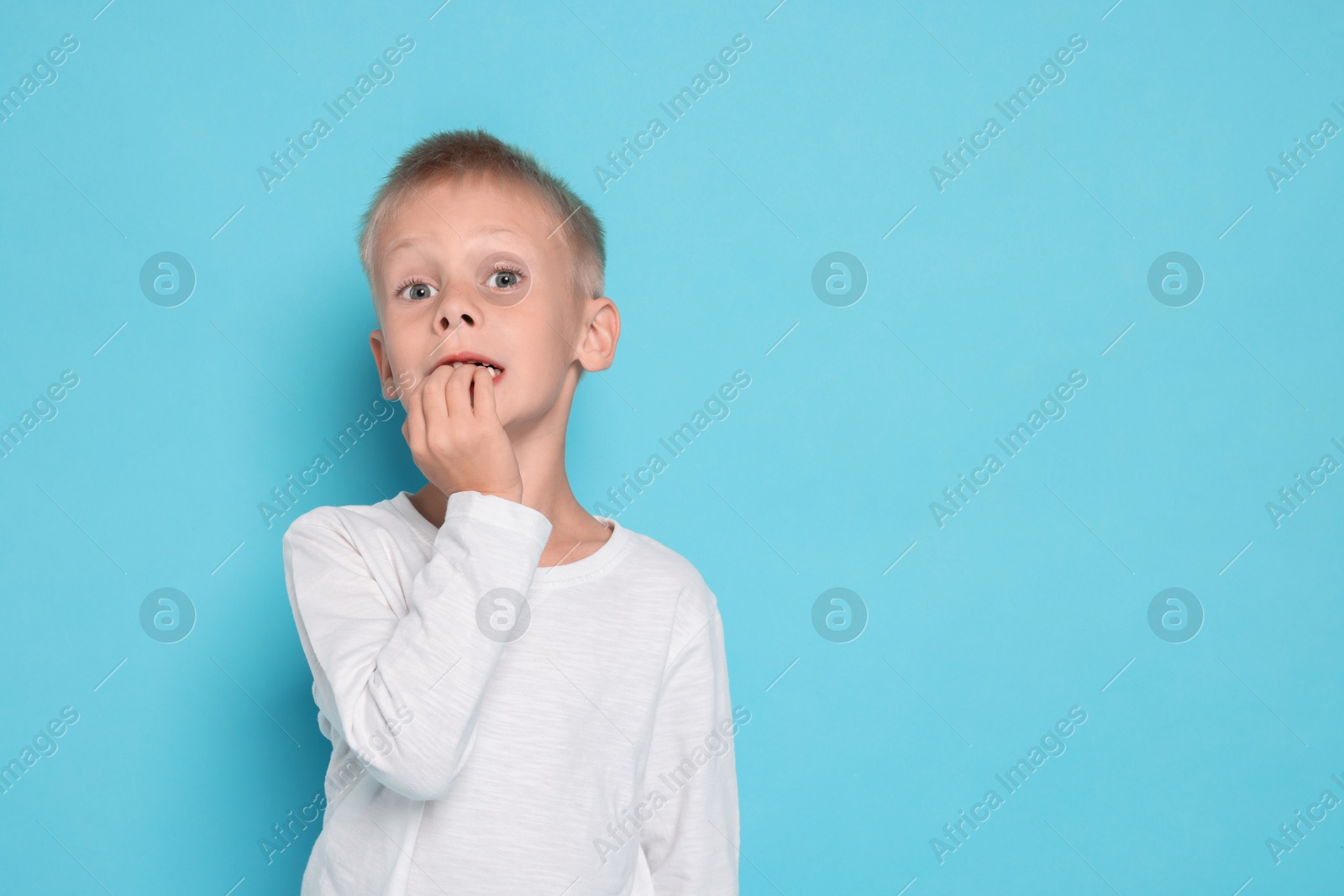 Photo of Scared little boy on light blue background. Space for text