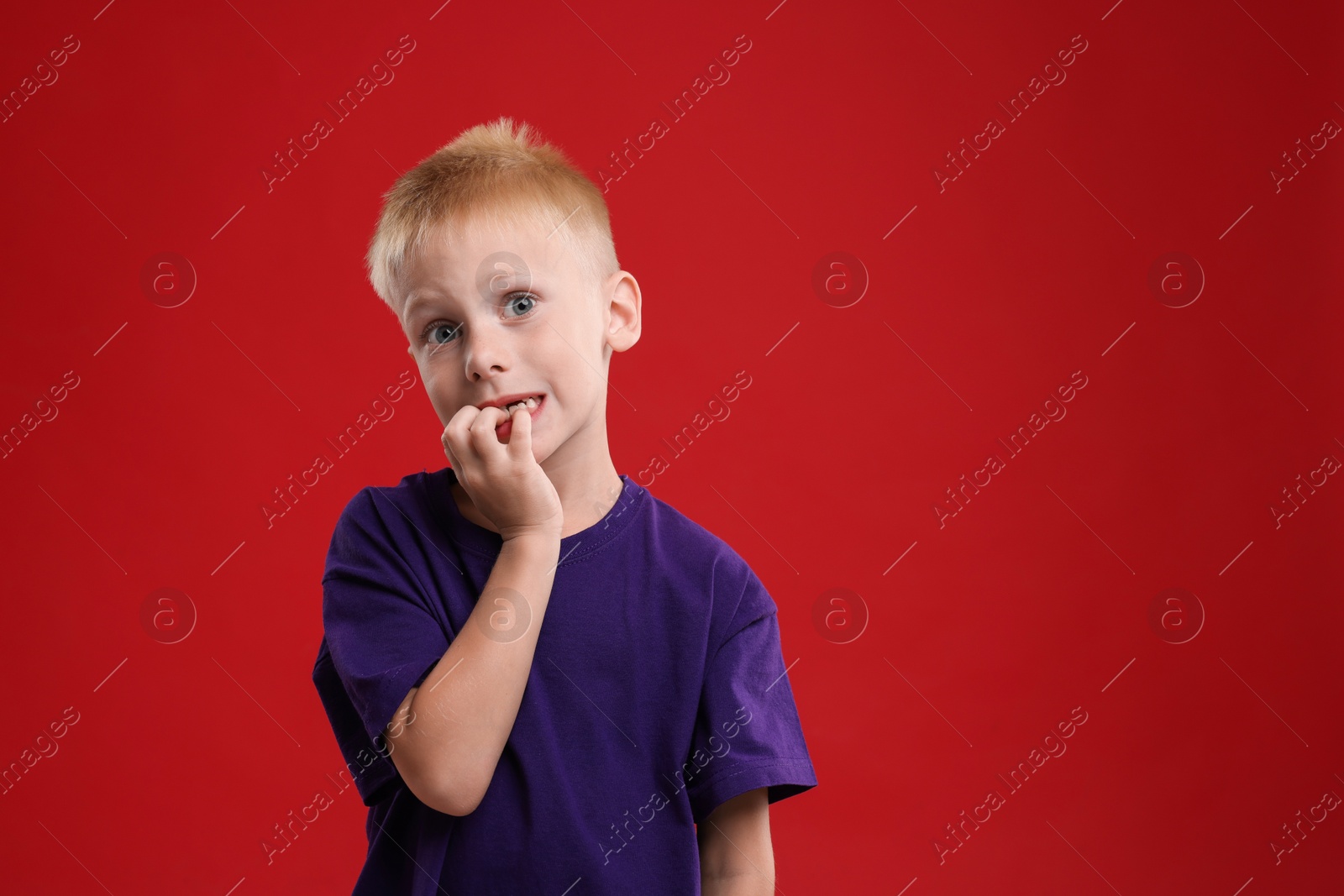 Photo of Scared little boy on red background. Space for text