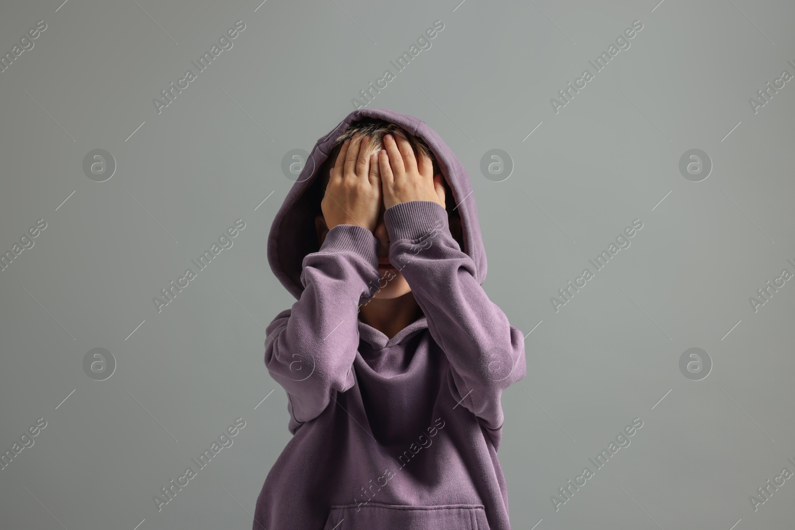 Photo of Scared little boy covering face with hands on grey background