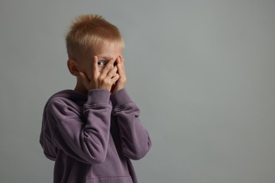 Scared little boy hiding on grey background. Space for text