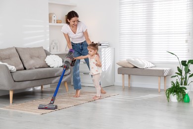 Smiling young woman and her daughter cleaning floor with cordless vacuum cleaner at home