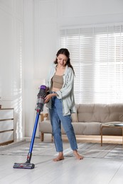 Photo of Smiling young woman cleaning floor with cordless vacuum cleaner at home