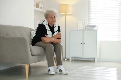 Loneliness concept. Sad senior woman sitting on sofa at home