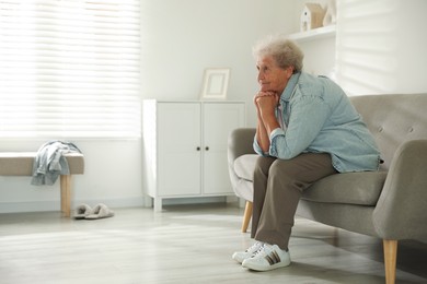 Photo of Loneliness concept. Sad senior woman sitting on sofa at home