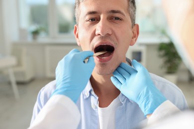 Photo of Doctor examining man's throat with tongue depressor in clinic