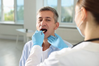 Photo of Doctor examining man's throat with tongue depressor in clinic