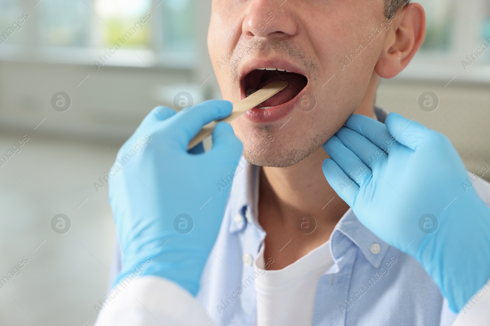 Photo of Doctor examining man's throat with tongue depressor in clinic, closeup