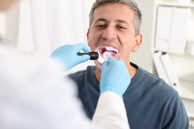 Doctor examining man's throat with flashlight in clinic